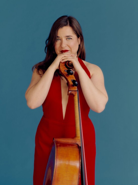 a woman in a red dress rests both hands on the scroll of a cello