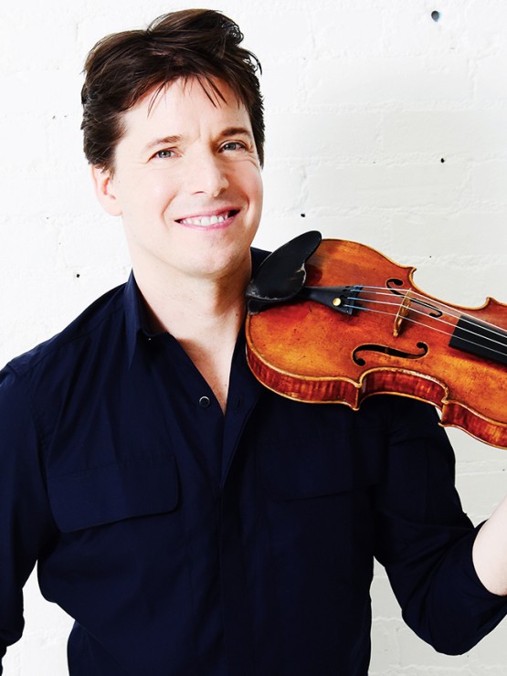 a white man in a navy blue button down shirt smiles as he hold a violin to his chin.