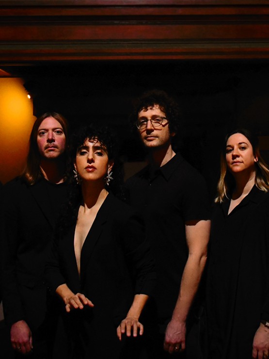 seven musicians in a performance space with warm amber light. some are turned to the side but all look at the camera