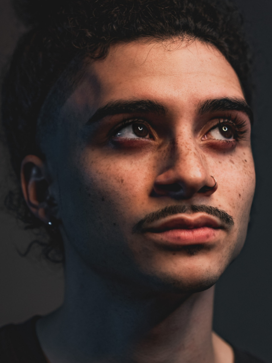 a chiaroscuro portrait of a young man with dark eyes, intense eyebrows, freckles, and short facial hair. 