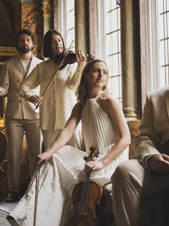 four musicians stand holding their instruments in a glass-walled stairwell