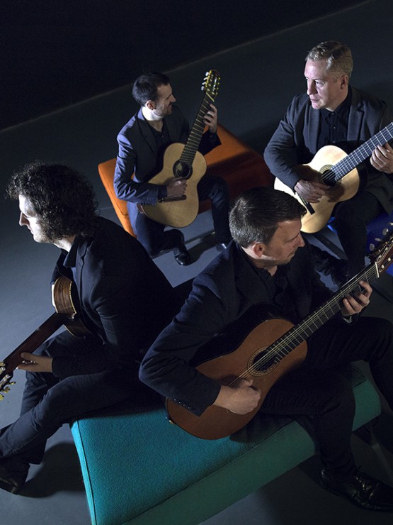 from above, with blue light casting shadows, four white men sit on the sides of a square box, turned in various directions