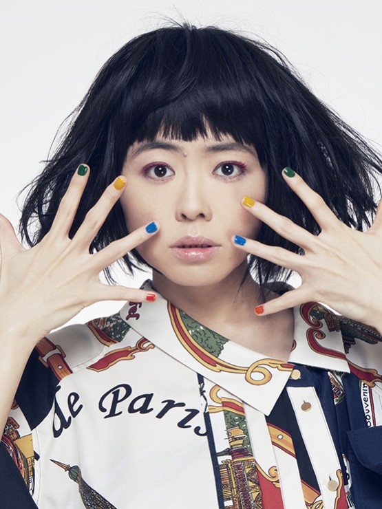 Hiromi, an Asian woman with dark hair wearing a patterned shirt holding her hands in front of her face in front of a white background. 