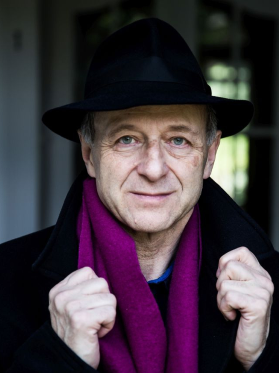 a hungarian man with a felt hat and a bright violet scarf grasps the collars of his black wool overcoat