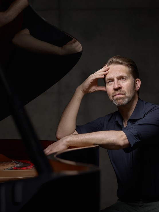 a norwegian man rests his elbow on the open rim of a piano