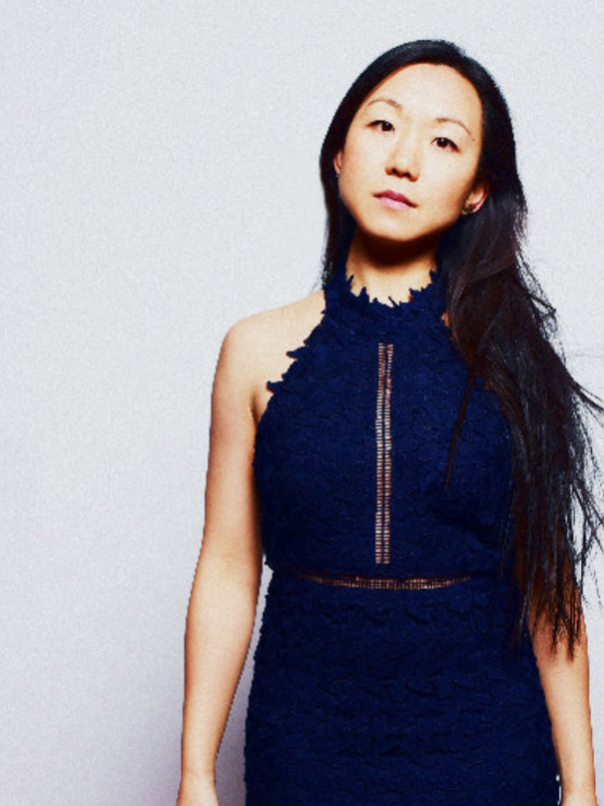 an asian woman, with long wavy hair, tilts her head slightly to the side, as she stands with her arms at her sides in a navy blue halter neck dress