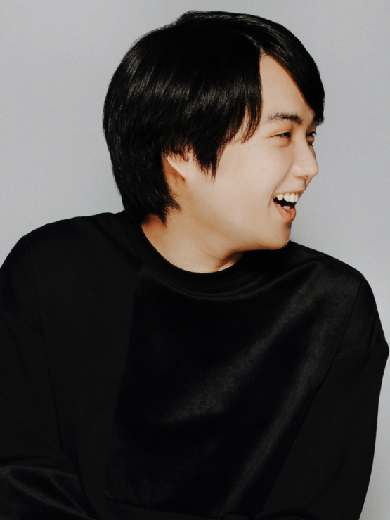 a japanese man in his 20s turns his head to the side with a broad smile