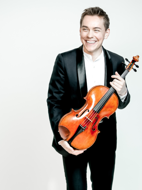 a brown-haired white man in his late 20s smiles as he hugs his viola