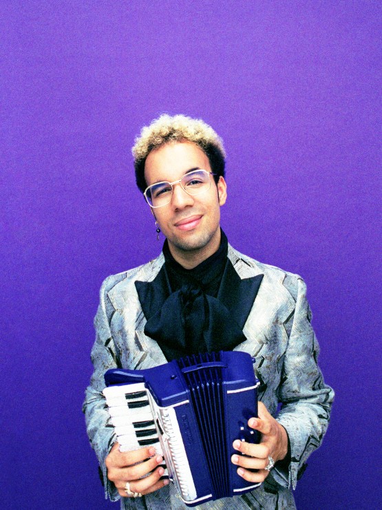 a young multiracial man with bleached blond hair on top wears a silver formal jacket with black lapels