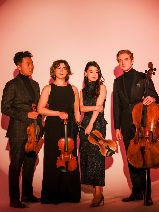in a warm ombre spotlight, a string quartet wearing all black holds their instruments