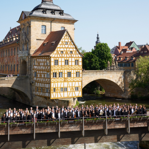 an orchestra lined up across a bridge with a yellow half-timbered building in the background