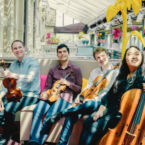 a string quartet with their instruments in a glass-roofed atrium hung with colorful artwork