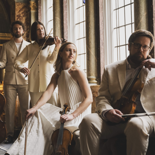 four musicians stand holding their instruments in a glass-walled stairwell