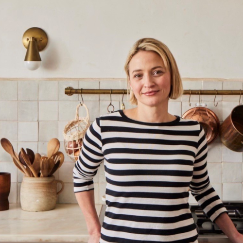 a blonde white woman with short hair and a black and white striped top stands in a bright kitchen