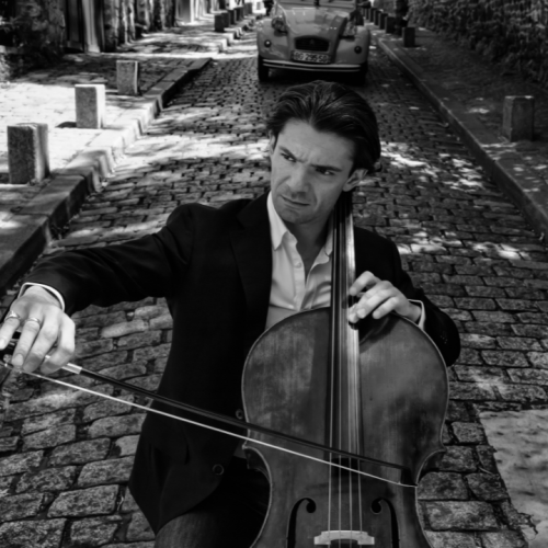 a black and white image of a man playing a cello on a shady european street