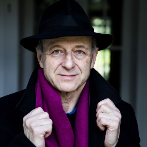a hungarian man with a felt hat and a bright violet scarf grasps the collars of his black wool overcoat