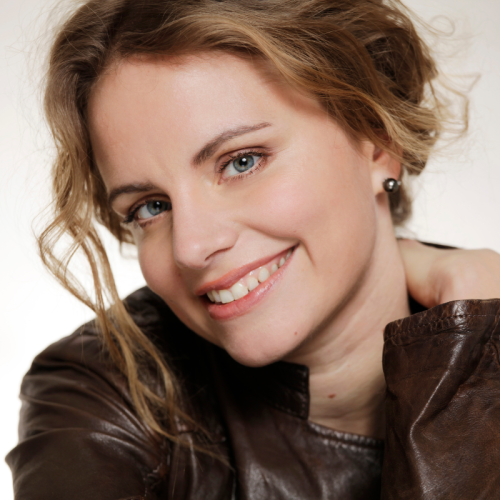 a white woman in her 30s with dark blonde hair smiles in a 3/4 view, one hand on her shoulder