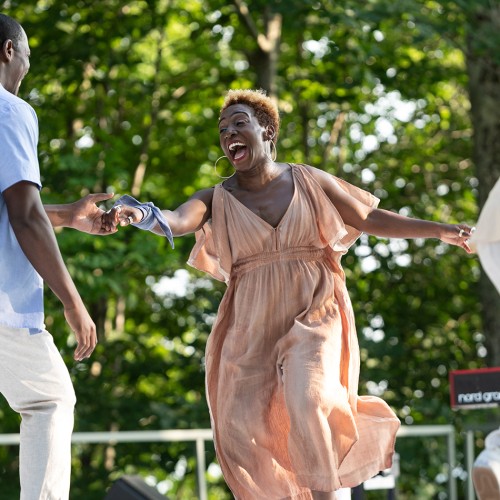 a joyous black woman in motion smiles broadly as she grasps her dance partner's hand