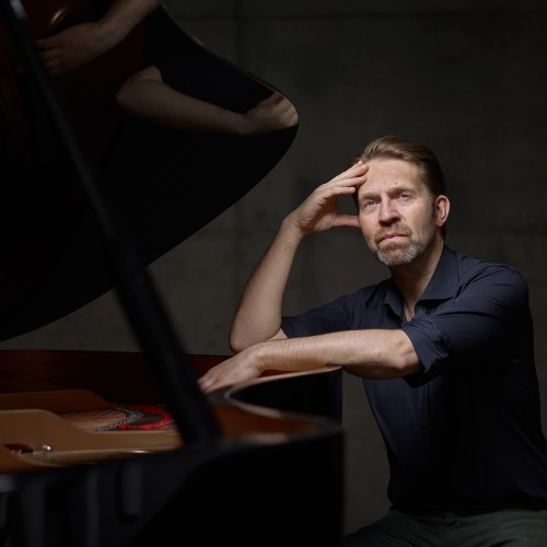 a norwegian man rests his elbow on the open rim of a piano