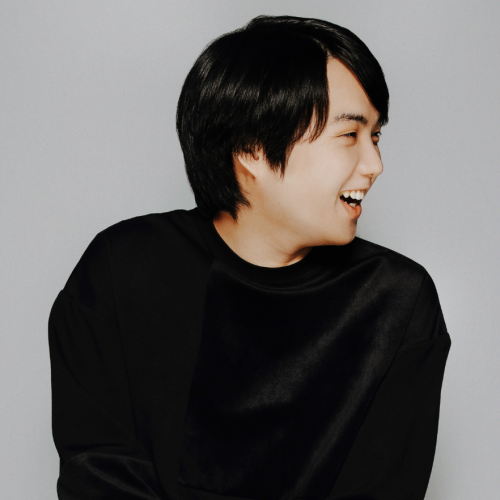 a japanese man in his 20s turns his head to the side with a broad smile