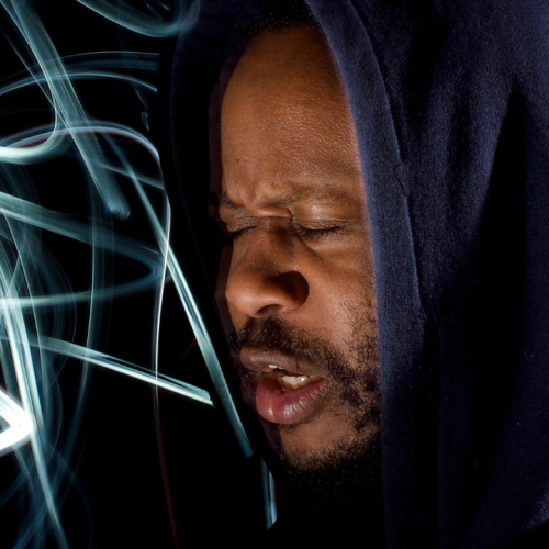 a black man, his eyes closed, his hood up, with abstract swirls of light that looks like graffitti emanating from his mouth