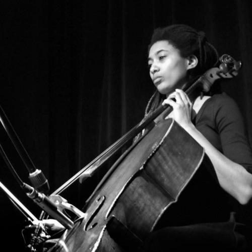 a black and white photo, taken from a low angle, of a Black woman playing the cello