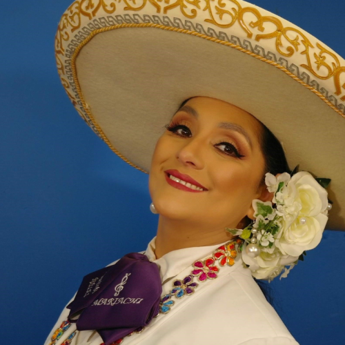 a mexican woman with flowers in her hair and a cream-colored embroidered sombrero leans back at the waist with a smile