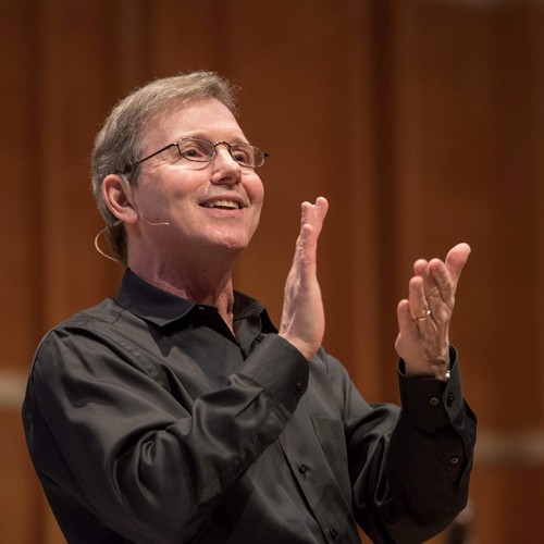 a smiling white man in a black shirt claps his hands 