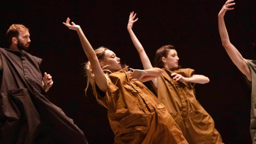 dancers in earth-toned rompers lean back in unison, one arm arced over their heads