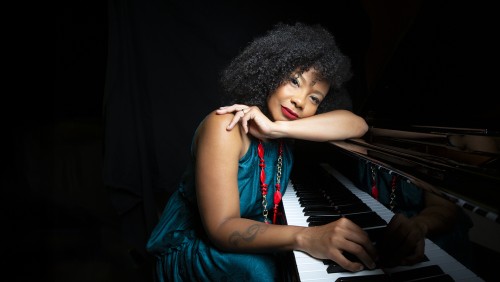 an afro-cuban woman leans over the keys of a piano: she wears a richly colored turquoise and magenta dress