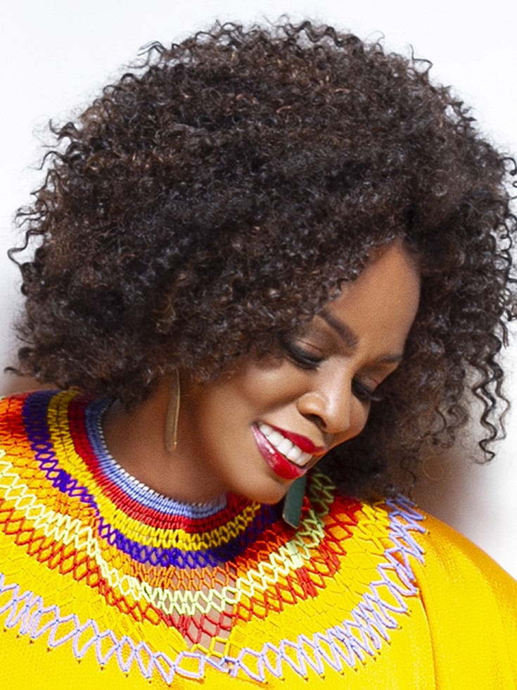Dianne Reeves smiles as she looks down. She wears a flowing, vivid yellow gown with small beading at the yoke