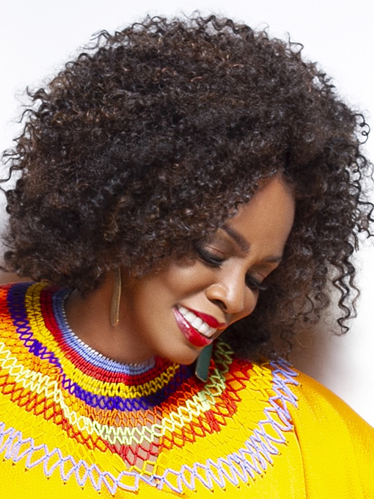 Dianne Reeves smiles as she looks down. She wears a flowing, vivid yellow gown with small beading at the yoke