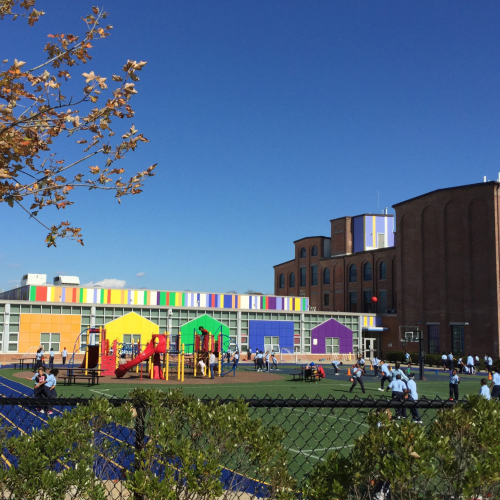 a playing field and a school in a renovated industrial building. silhouetted houses and buildings in rainbow colors decorate the wall.