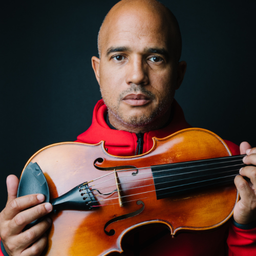 a bald black man in a red hoodie holds his violin toward us