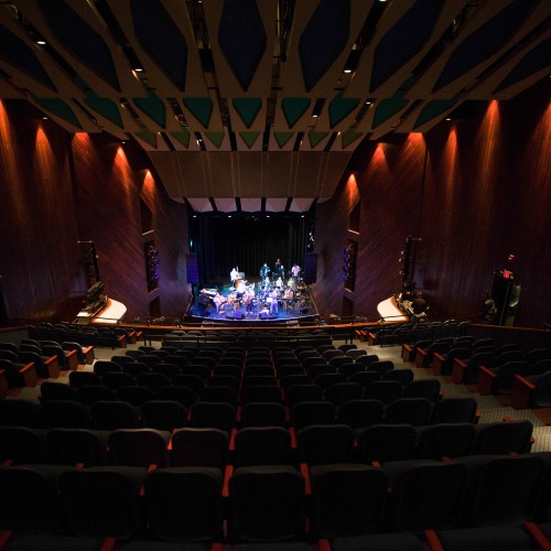 A view from the balcony, a large ensemble plays in a dimly lit auditorium
