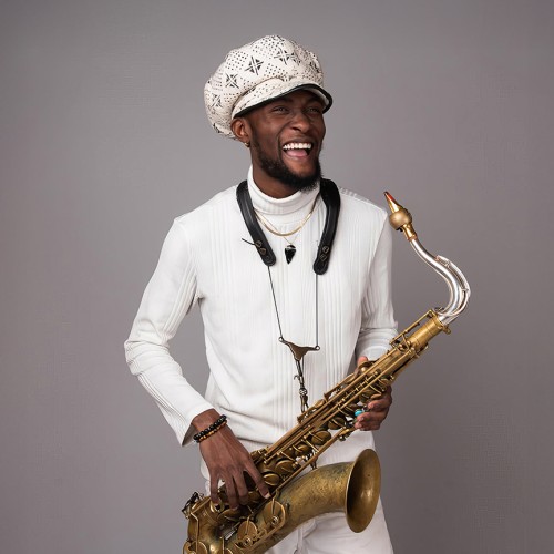 A young black man wearing an oversized paperboy cap stands holding a tenor saxophone with a vintage finish. 