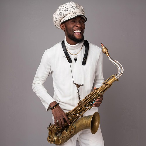 A young black man wearing an oversized paperboy cap stands holding a tenor saxophone with a vintage finish. 