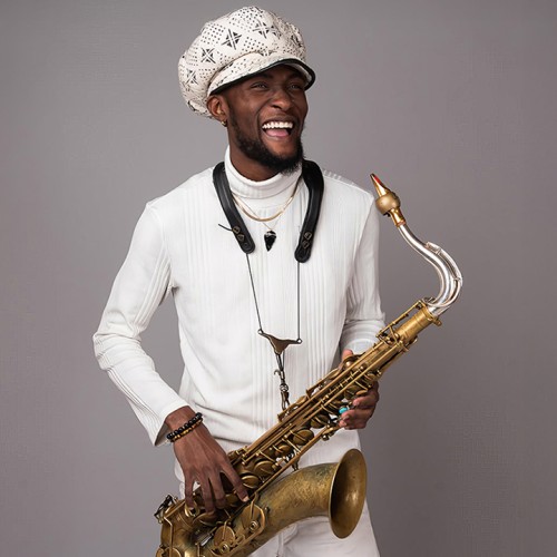 A young black man wearing an oversized paperboy cap stands holding a tenor saxophone with a vintage finish. 