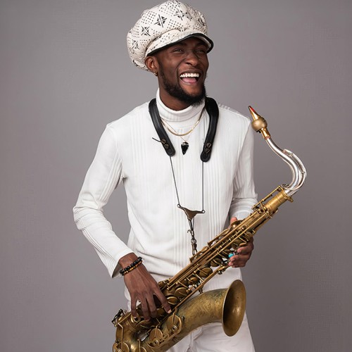 A young black man wearing an oversized paperboy cap stands holding a tenor saxophone with a vintage finish. 