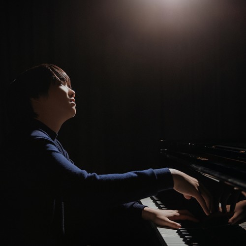 in an illuminated silhouette, a young japanese man plays the piano