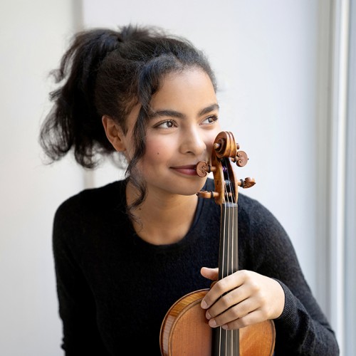 a multiracial teen girl with curly hair in a ponytail holds her the scroll of her violin to her cheek as she looks to the side