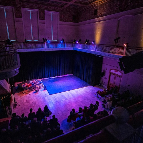 A small room with a balcony and flat wooden stage lit in purple