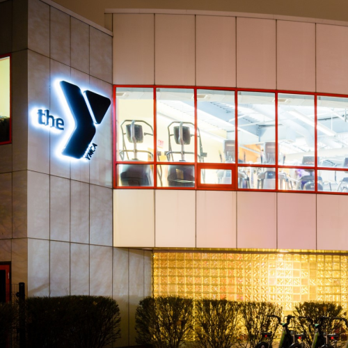 the exterior of the roxbury YMCA, with a curved bank of windows looking into a bright workout studio full of fitness machines