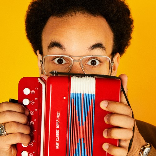 behind a tiny read concertina, the expressive eyes and raised eyebrows of a young multiracial man with short natural hair. We can't see his mouth, but his expression is happy.