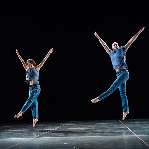two members of Trisha Brown Dance Company wear blue bodysuits, leaping into the air with arms extended