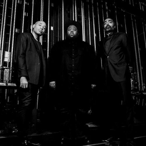 A black and white photo of three stoic black men standing backstage in front of backstage rigging 