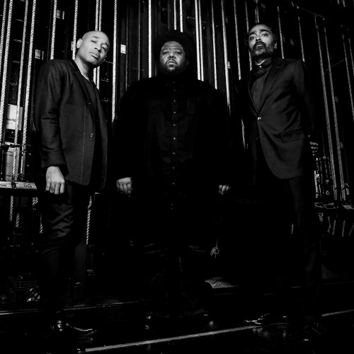A black and white photo of three stoic black men standing backstage in front of backstage rigging 