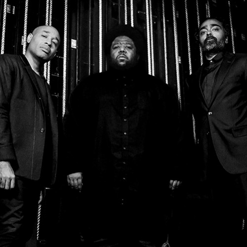 A black and white photo of three stoic black men standing backstage in front of backstage rigging 