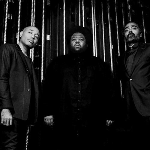 A black and white photo of three stoic black men standing backstage in front of backstage rigging 