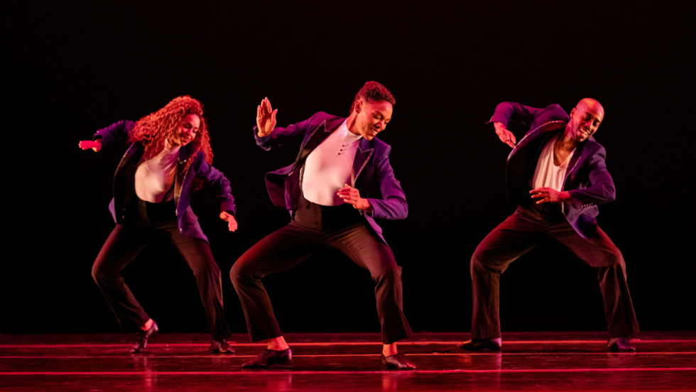 three dancers, both arms bent and slightly extended, slide to their right, 